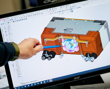 Engineer pointing at a 3D mechanical model on a CAD software displayed on a computer screen.